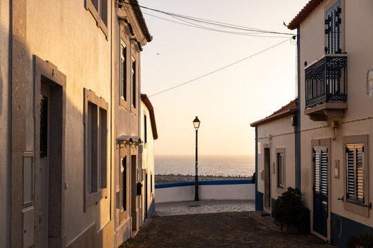 view from narrow residential cobblestone street in Ericeira, Portugal looking towards ocean during golden hour