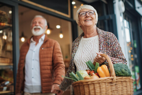 Senior couple walking holding hands carrying grocery basket outside local market store together