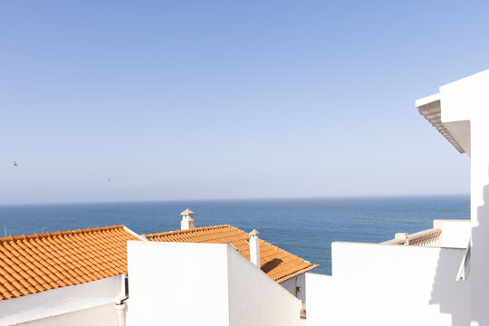 white architectural house by the sea with orange tiled roof with blue ocean in the background, minimal, negative space