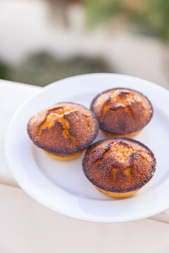 3 Ouricos, portugese local specialty sweet made from almond flour, sugar, eggs, and citrus zest, shaped like a small round bun with a caramelized crust on a plate with a soft focus garden background 