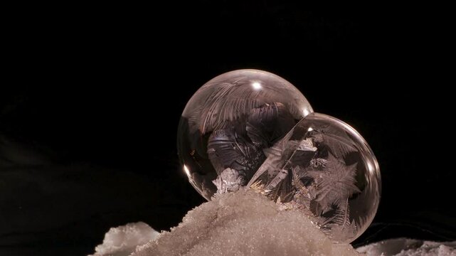 Macro time lapse of ice crystals forming inside soap bubbles sitting on a pile of snow against a black background.