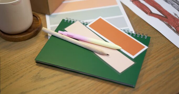 Camera is shifting focus and centering green spiral notebook with pens on desk to highlight design