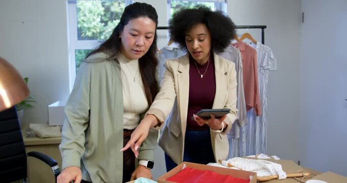 African American, Asian female team holding tablet gesturing at samples at table choosing products