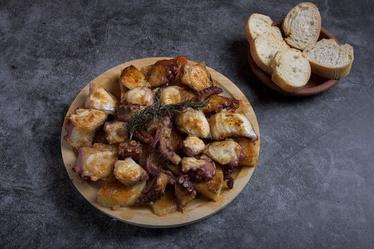 Traditional Spanish octopus tapa served on a wooden plate with potatoes, olive oil, lemon, bread, and spices on a dark background