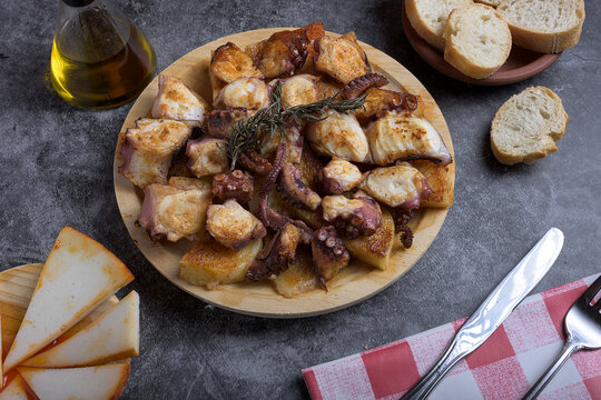 Traditional Spanish octopus tapa served on a wooden plate with potatoes, olive oil, lemon, bread, and spices on a dark background