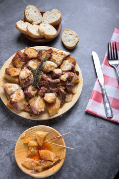 Traditional Spanish octopus tapa served on a wooden plate with potatoes, olive oil, lemon, bread, and spices on a dark background
