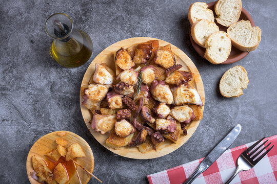Traditional Spanish octopus tapa served on a wooden plate with potatoes, olive oil, lemon, bread, and spices on a dark background