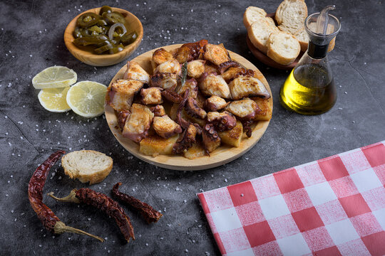 Traditional Spanish octopus tapa served on a wooden plate with potatoes, olive oil, lemon, bread, and spices on a dark background