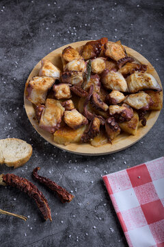 Traditional Spanish octopus tapa served on a wooden plate with potatoes, olive oil, lemon, bread, and spices on a dark background