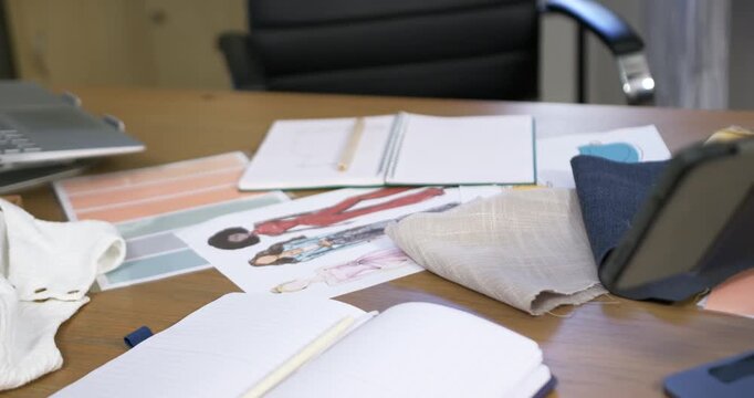 Low-angle camera is pushing, focusing, showing note, sketches, swatches on table for design review