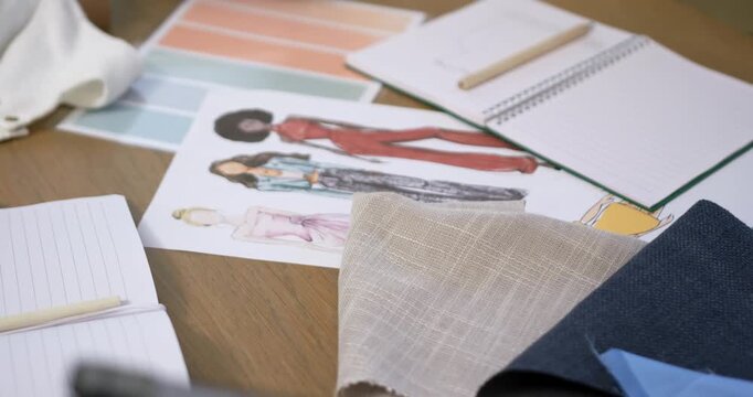 Camera is pulling back and refocusing on wooden table, revealing fashion sketch sheet and palette