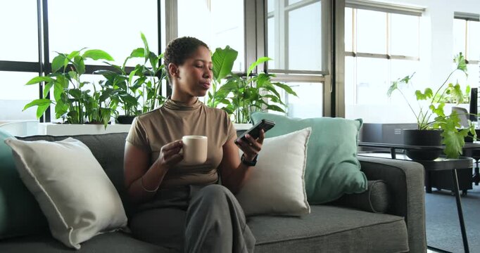 African woman in tan top in office lounge seeing phone, scrolling to read message, holding mug