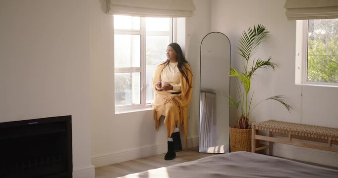 Adult African American woman sitting on sill in mustard shawl sipping mug as sunlight drawing gaze