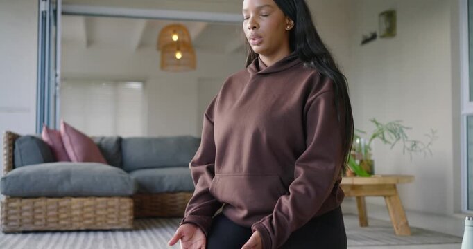 African American woman kneeling on mat at home, palms-up eyes closed, practicing breathing to calm