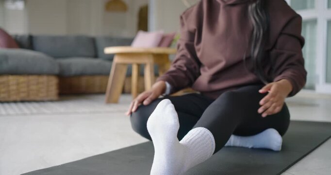 Post warmup African American woman doing seated stretches on black mat at home hoodie white-sock