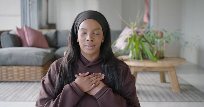 African American woman wearing hoodie at home placing hands over chest, breathing calmly, smiling