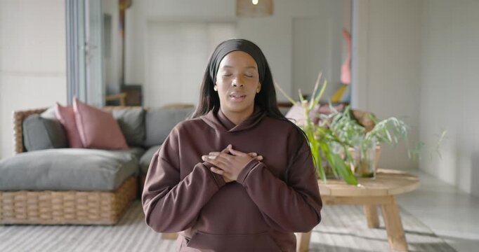 African American woman breathing, opening eyes, smiling, kneeling on yoga mat at home with bottle