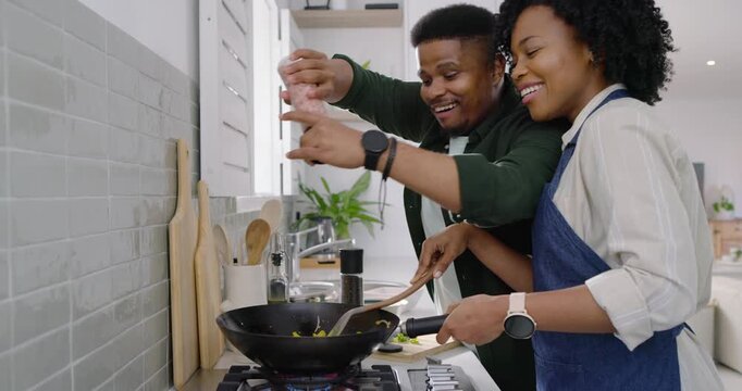African American couple cooking at stove woman in apron stirring wok man leaning grinding pepper