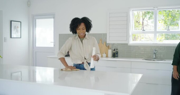 Couple wiping kitchen island, woman grabbing spray bottle and wiping as man holding cloth smiling