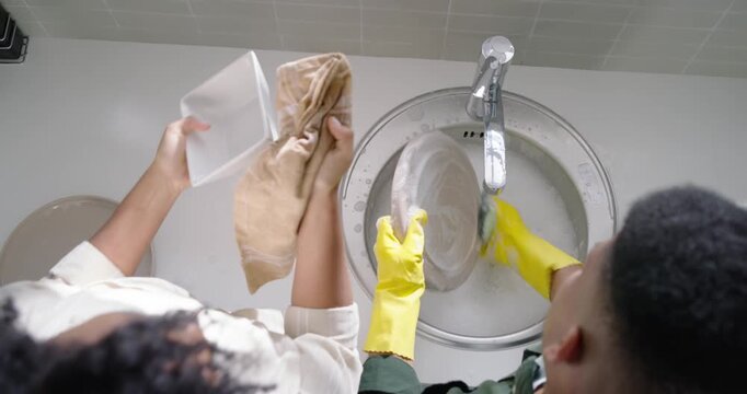African American couple washing dishes right wearing gloves placing plate in soapy sink for drying