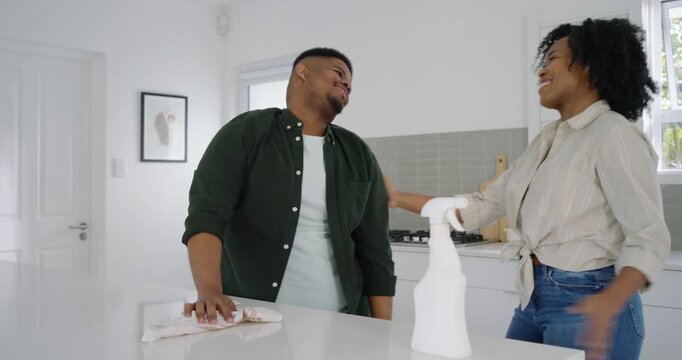 African couple man wiping kitchen island with rag near white spray bottle, woman reaching, flirting