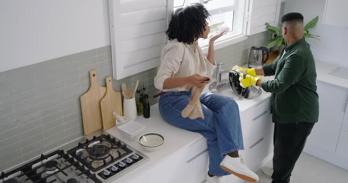 African American couple washing, drying dishes at sink, man rinsing with yellow gloves splashing