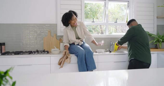 African American couple at kitchen sink, woman reaching bag, man splashing, yellow gloves, hugging