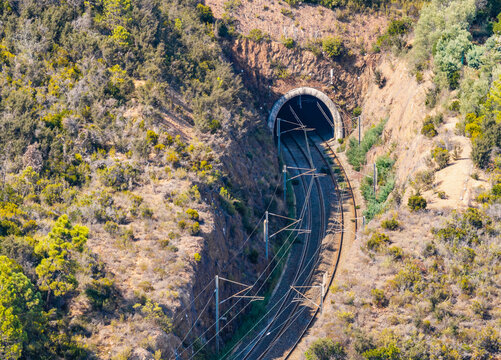 Aerial view of an electrified double-track railway curving into a mountain tunnel through a rocky Mediterranean landscape in Saint-Raphael, Provence-Alpes-Cote d'Azur, France.