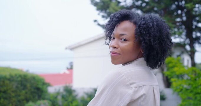 African American adult woman in beige shirt turning toward camera as camera nears, laughing in yard