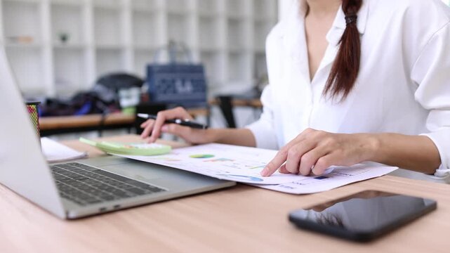 Asian businesswoman calculating financial data and analyzing reports in office.