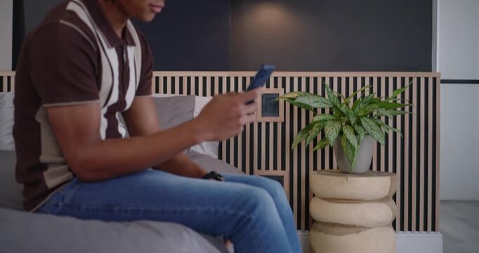Man in his 20s brown-beanie settling on sofa, scrolling blue-case smartphone, smiling at messages