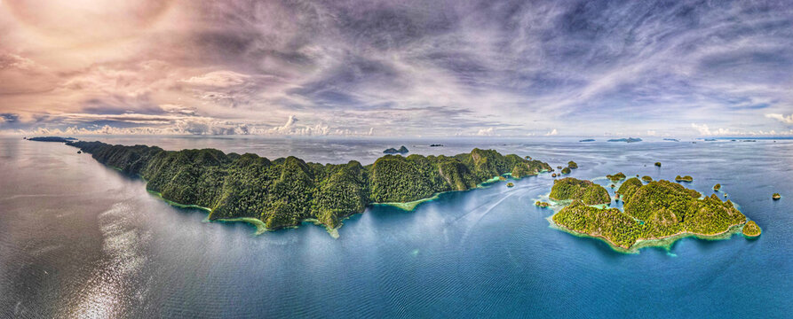 Aerial view of Raja Ampat Regency with lush green islands surrounded by turquoise waters under a dramatic sky, Southwest Papua, Indonesia.