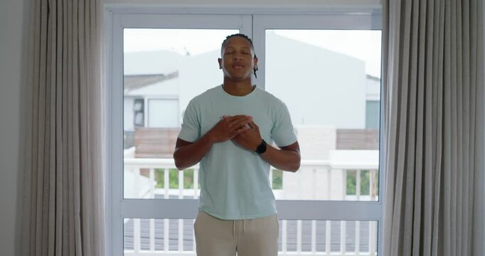 African adult male standing before glass door closing eyes and clasping chest, calming with watch