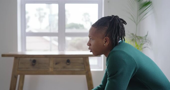Adult African male rubbing forehead, thinking, clasping hands on woven bench by window, copy space