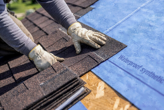 Professional roofing worker installing asphalt shingles with protective gloves on residential roof