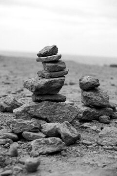 Zwei sorgf&auml;ltig gestapelte Steinm&auml;nnchen (Steinpyramiden) auf einem kargen, steinigen Boden unter hellem Himmel in Schwarz-Wei&szlig;.