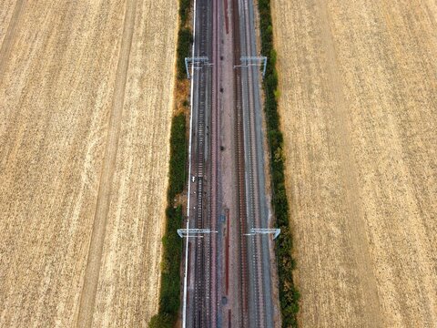 Aerial view of railway tracks running through golden wheat fields in the countryside in Finedon, England, United Kingdom.