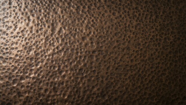 Close-up texture of hammered dark bronze metal with a rough, bumpy surface and warm lighting.