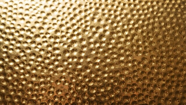 Close-up textured gold surface with hammered dimples, creating a shimmering metallic background.
