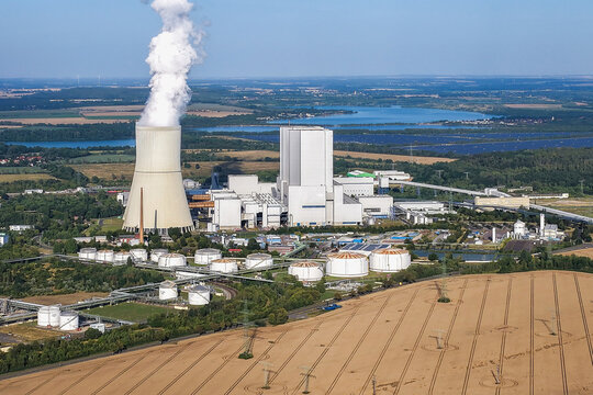 Aerial view of the Lippendorf Power Station with its cooling tower emitting steam, surrounded by industrial infrastructure, storage tanks, and fields in Leipzig, Saxony, Germany.