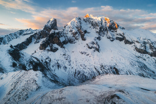 Aerial view of Passo Giau featuring snow-covered mountain peaks illuminated by golden hour light in the dramatic alpine landscape of Colle Santa Lucia, Veneto, Italy.