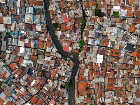 Aerial view of a dense urban neighborhood featuring a narrow canal winding through tightly packed houses with terracotta rooftops in Bandung, West Java, Indonesia.
