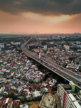 Aerial view of the Pasupati Bridge spanning over the dense urban landscape with traffic flowing on the elevated highway under a dramatic sunset sky in Bandung, West Java, Indonesia.