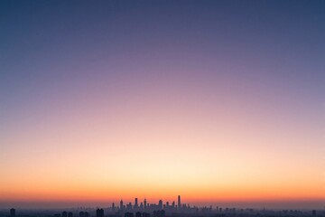 Fototapeta premium Minimalist city skyline at dawn with pastel colors. Soft pink, orange hues blend into vast sky above urban buildings. Quiet morning landscape offers serene atmosphere, huge copy space for design
