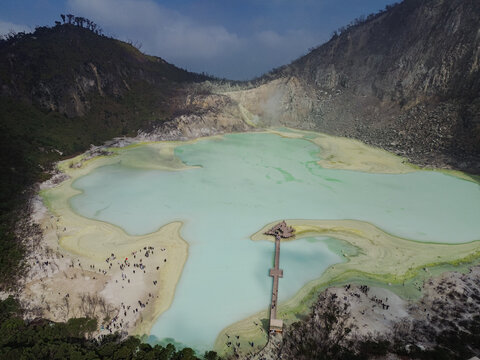 Aerial view of Kawah Putih Ciwidey, a volcanic crater lake with turquoise water, rugged cliffs, a wooden pier, and visitors on the shore Bandung, West Java, Indonesia.