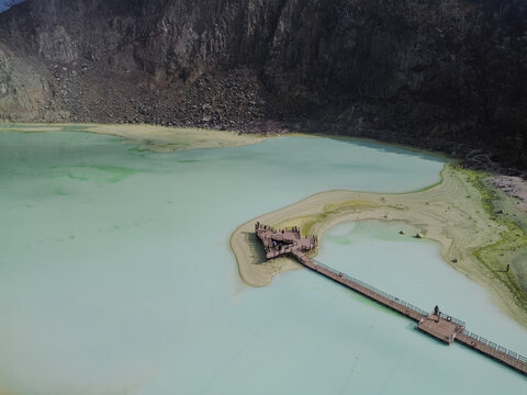 Aerial view of Kawah Putih Ciwidey, a volcanic crater lake with turquoise water, wooden boardwalk, and surrounding rocky cliffs, Bandung, West Java, Indonesia.