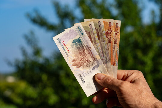Man holding Cambodian riel banknotes in hand outdoors. Closeup of hand holding several Cambodian riel cash bills of different denominations against blurry green nature background