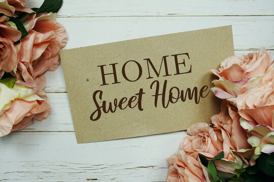 Home Sweet Home text on paper card with rose flowers bouquet on wooden background