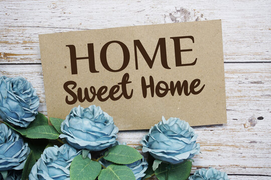 Home Sweet Home text on paper card with rose flowers bouquet on wooden background
