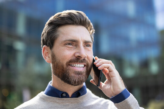 Close-up photo of a young man standing outside and smiling while talking on the phone